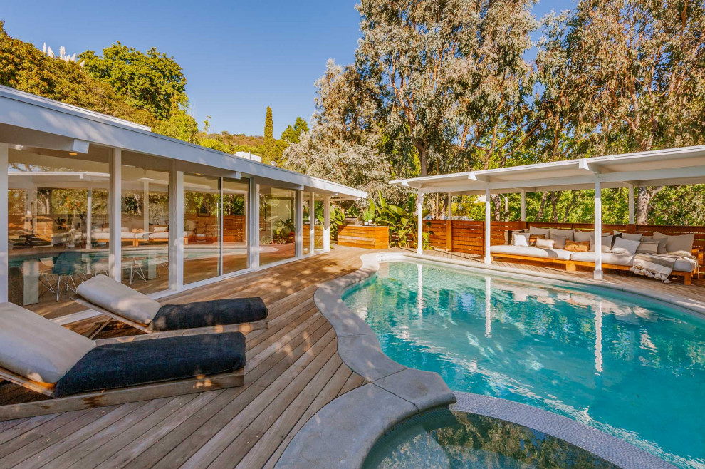 Cette image montre une grande piscine naturelle et arrière vintage sur mesure avec un bain bouillonnant et une terrasse en bois.