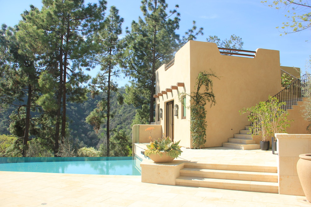 Exempel på en stor amerikansk anpassad infinitypool längs med huset, med poolhus och naturstensplattor