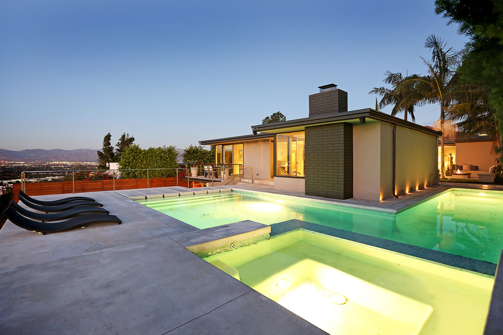 Esempio di una piscina moderna a "L" con lastre di cemento e una vasca idromassaggio