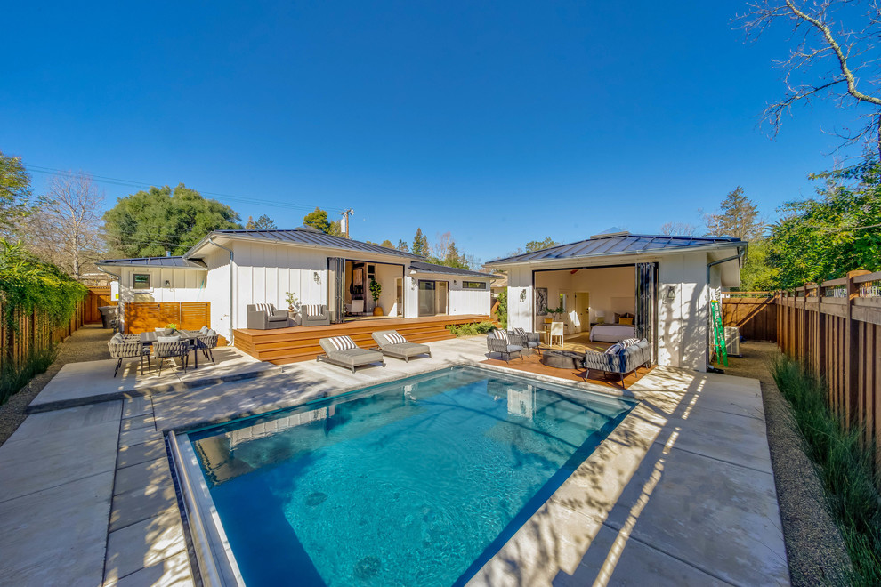 Ejemplo de casa de la piscina y piscina de estilo de casa de campo grande rectangular en patio trasero con losas de hormigón