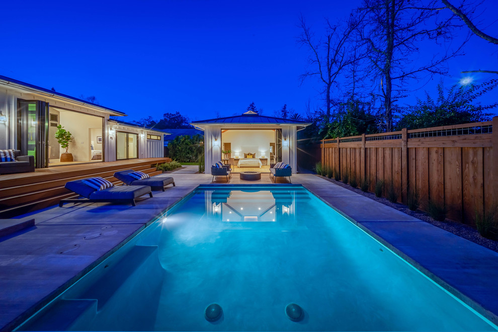 Ejemplo de casa de la piscina y piscina de estilo de casa de campo grande rectangular en patio trasero con losas de hormigón