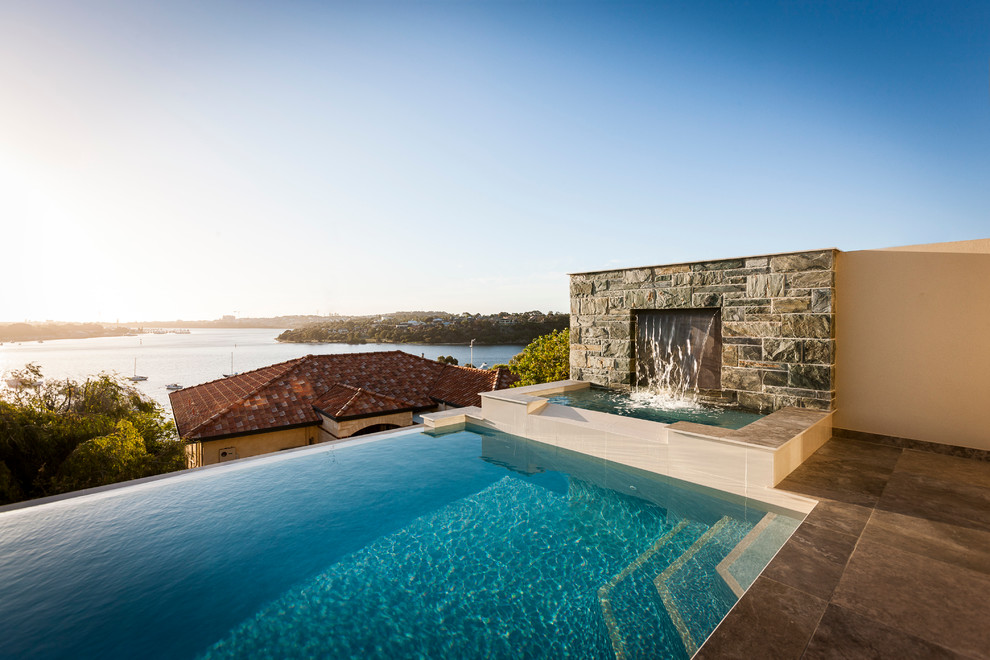 Immagine di una grande piscina a sfioro infinito minimal rettangolare dietro casa con fontane e pavimentazioni in pietra naturale
