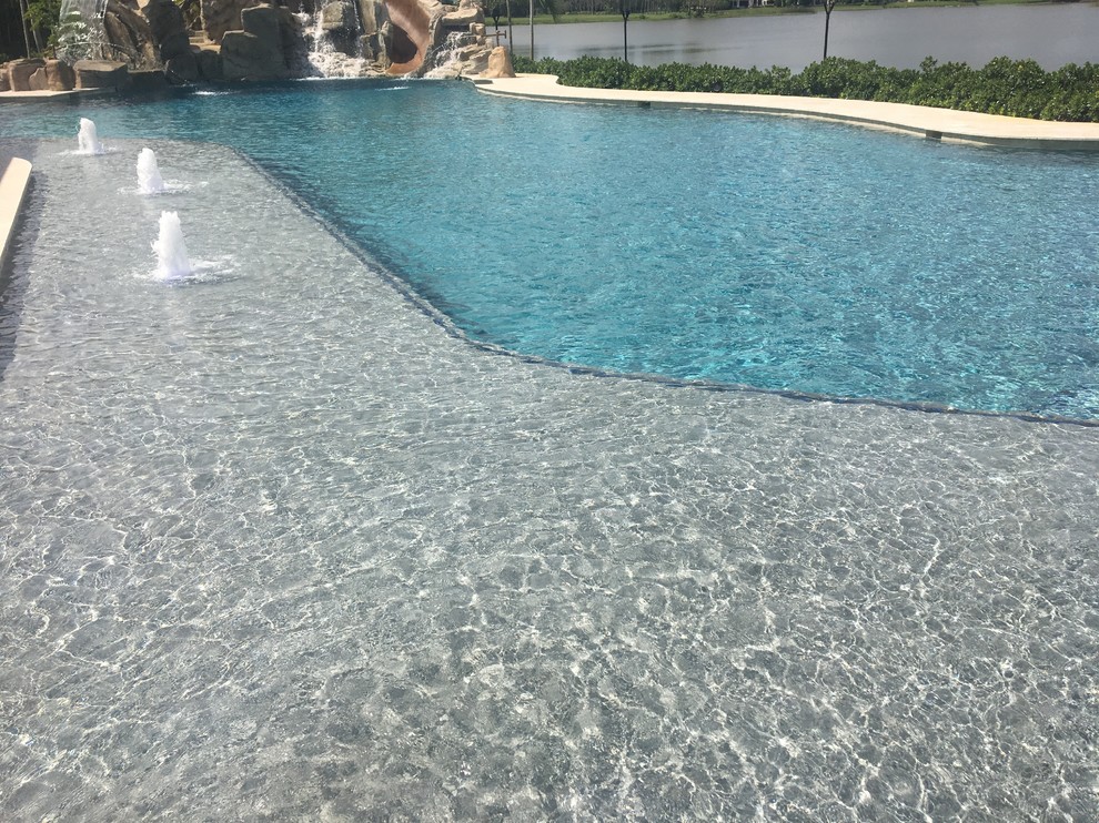 Idée de décoration pour une très grande piscine naturelle et arrière marine sur mesure avec un toboggan et des pavés en pierre naturelle.