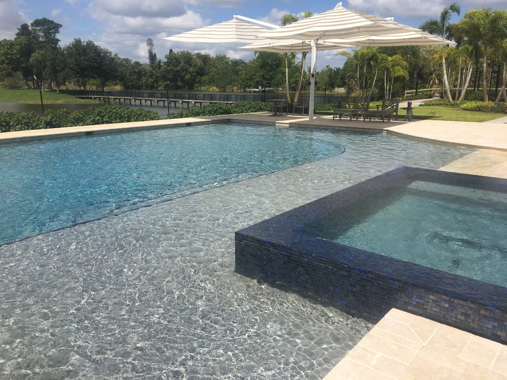 Design ideas for an expansive beach style back custom shaped natural swimming pool in Miami with a water slide and natural stone paving.