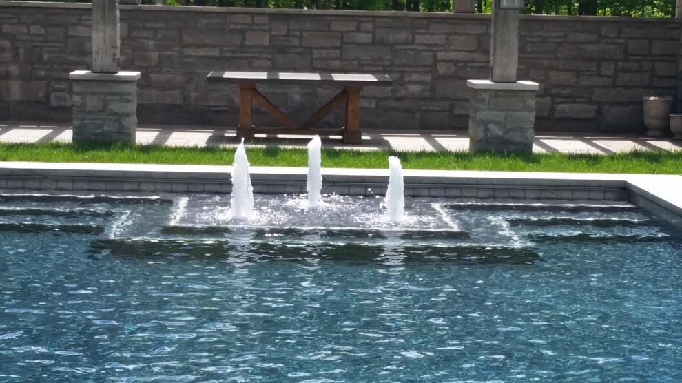 Diseño de piscina con fuente contemporánea grande rectangular en patio trasero con losas de hormigón