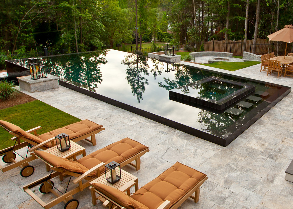 Example of a large trendy backyard stone and rectangular infinity hot tub design in Other