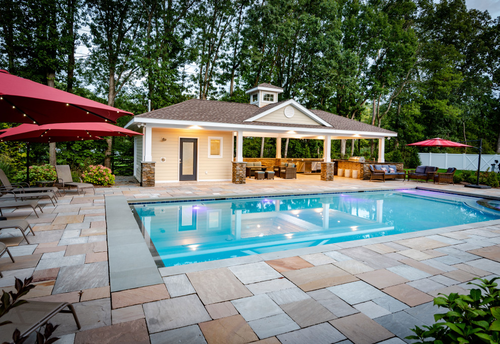 This is an example of a large coastal back rectangular swimming pool in New York with a pool house and natural stone paving.