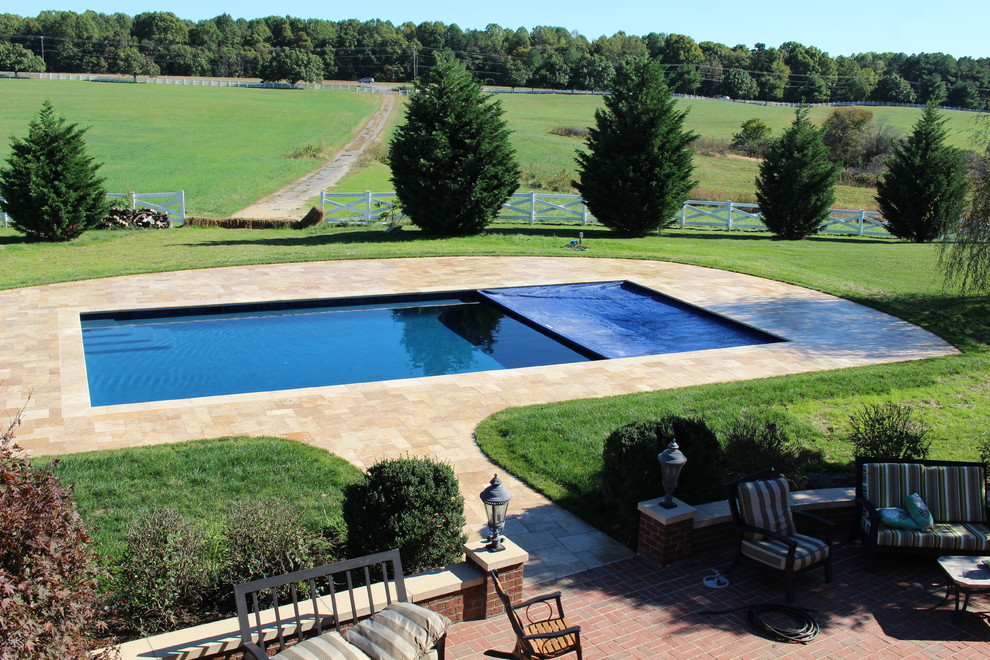 Ejemplo de piscina alargada tradicional grande rectangular en patio trasero con adoquines de piedra natural