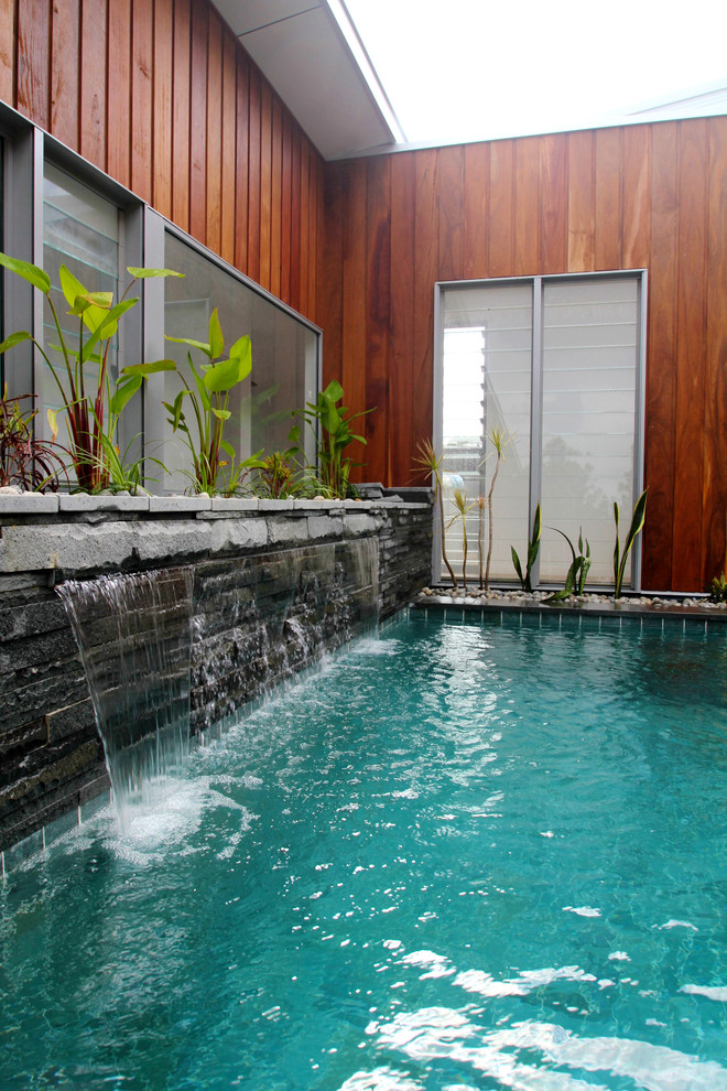 Imagen de piscina actual de tamaño medio rectangular en patio con adoquines de piedra natural