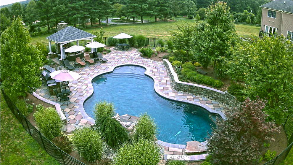 Réalisation d'une grande piscine arrière design sur mesure avec des pavés en pierre naturelle.