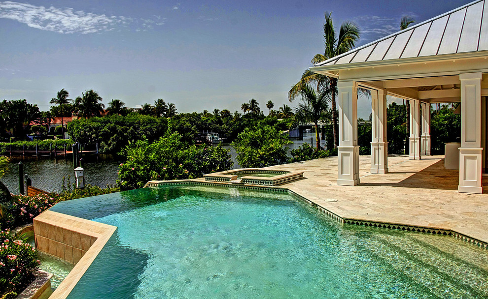 Idee per una piscina a sfioro infinito tropicale personalizzata di medie dimensioni e dietro casa con pavimentazioni in pietra naturale e una vasca idromassaggio