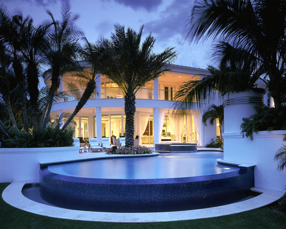 Foto di una grande piscina a sfioro infinito design personalizzata dietro casa con pavimentazioni in pietra naturale e una vasca idromassaggio