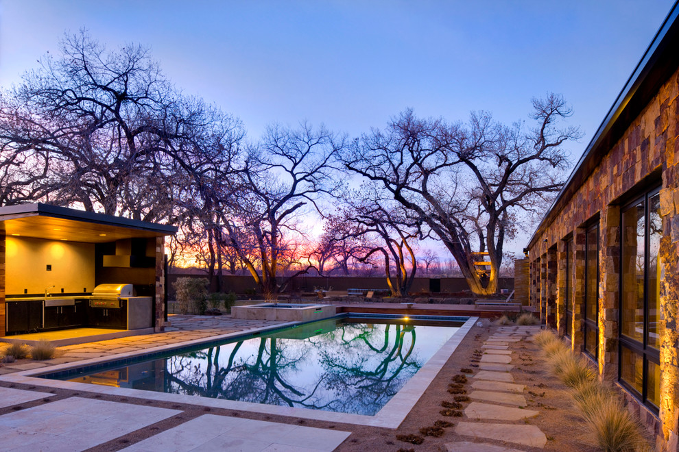 Foto di un'ampia piscina minimal rettangolare dietro casa con pavimentazioni in pietra naturale e una vasca idromassaggio