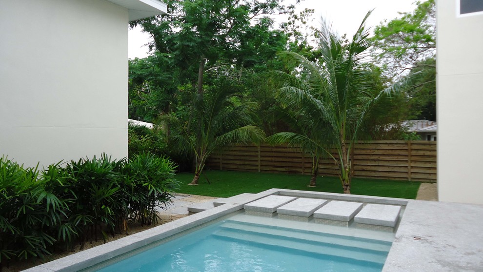 Foto di una piscina tropicale di medie dimensioni e dietro casa con fontane e lastre di cemento