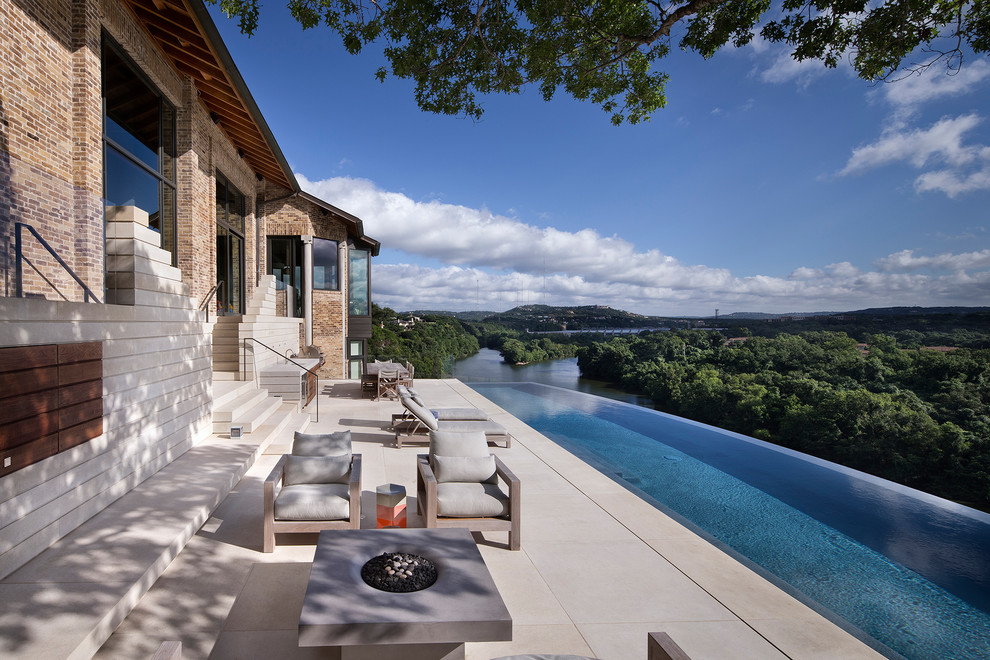 Immagine di una grande piscina a sfioro infinito contemporanea personalizzata dietro casa con pavimentazioni in pietra naturale