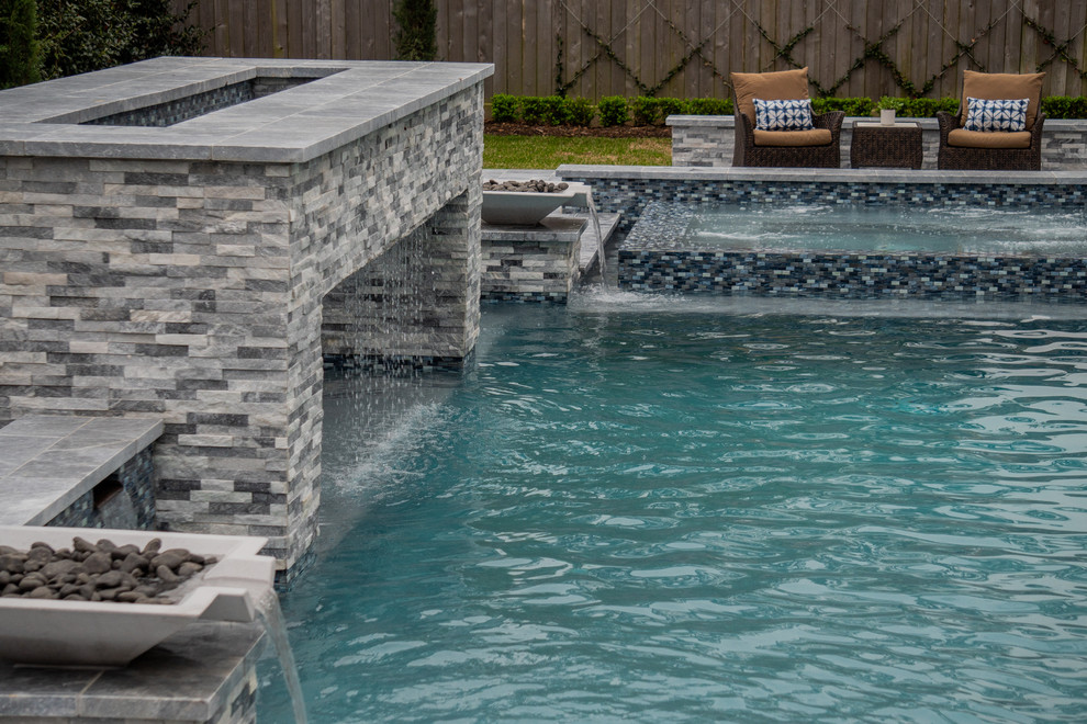 Modelo de piscina actual grande rectangular en patio trasero con adoquines de piedra natural