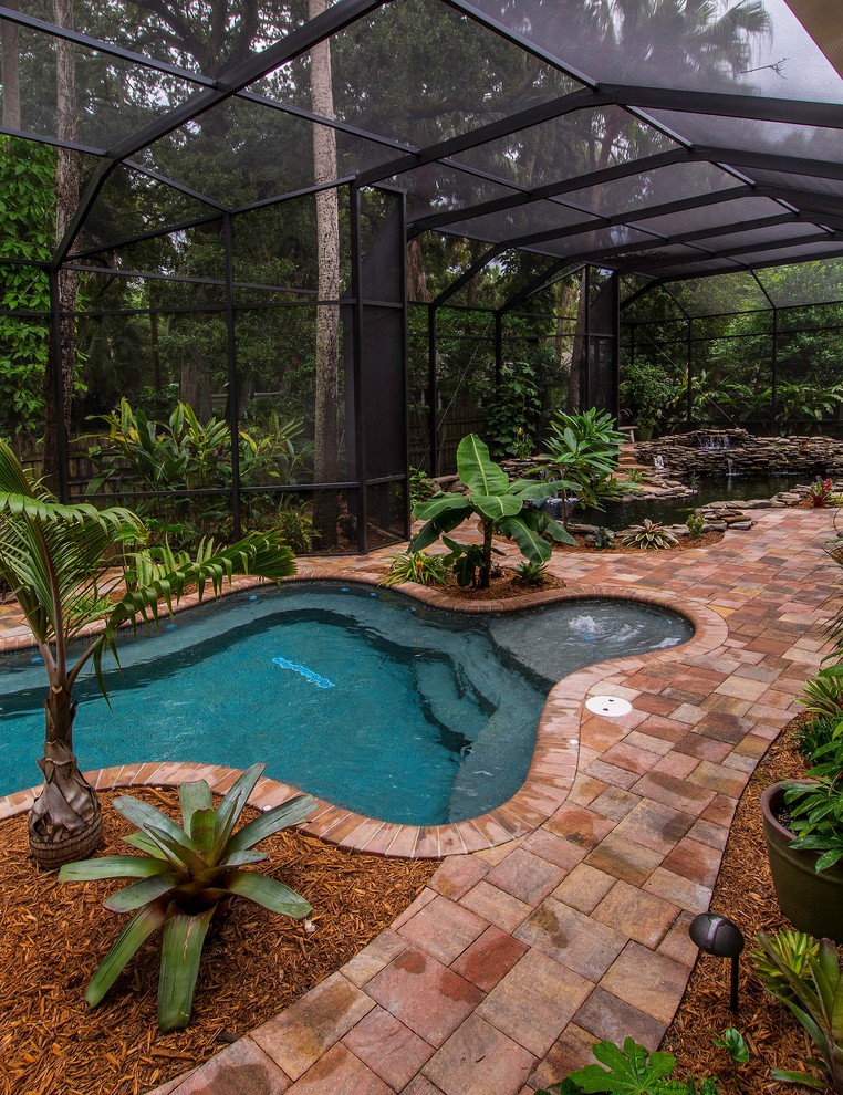 Foto de piscina con fuente natural tropical grande a medida en patio trasero con adoquines de ladrillo