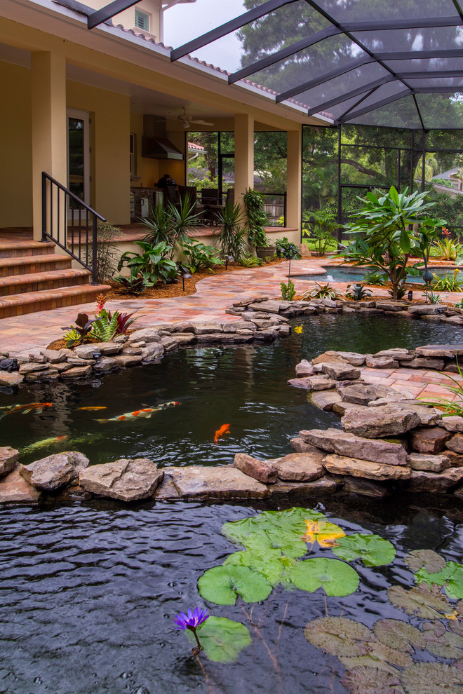 Ejemplo de piscina con fuente natural exótica grande a medida en patio trasero con adoquines de ladrillo