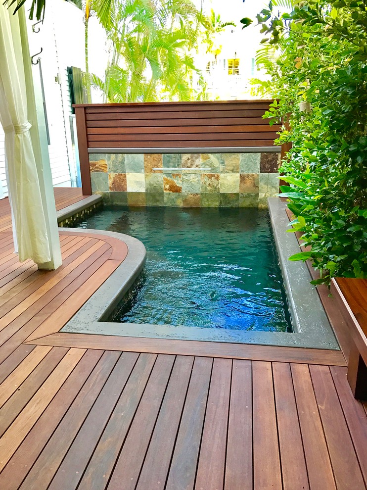 На фото: маленький угловой бассейн на заднем дворе в морском стиле с фонтаном и настилом для на участке и в саду