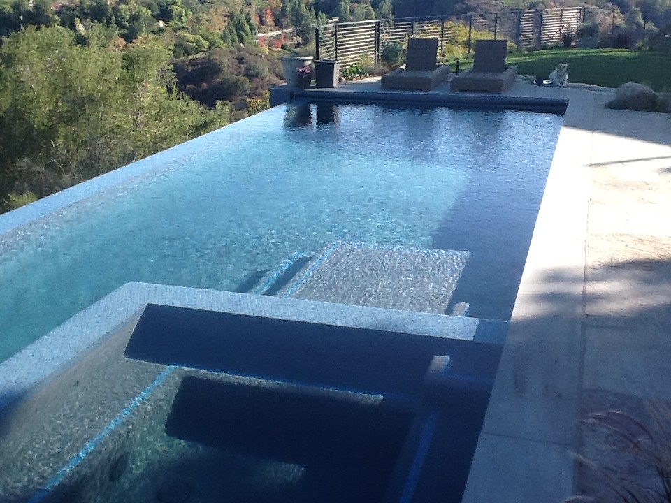 Immagine di una piscina a sfioro infinito country rettangolare di medie dimensioni e dietro casa con piastrelle