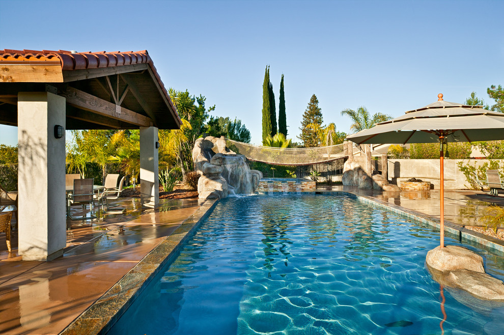 Medium sized world-inspired back rectangular lengths swimming pool in San Diego with a water slide and concrete slabs.
