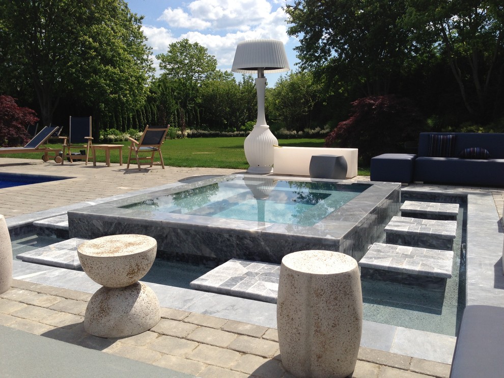 Diseño de piscina actual en patio trasero con adoquines de piedra natural