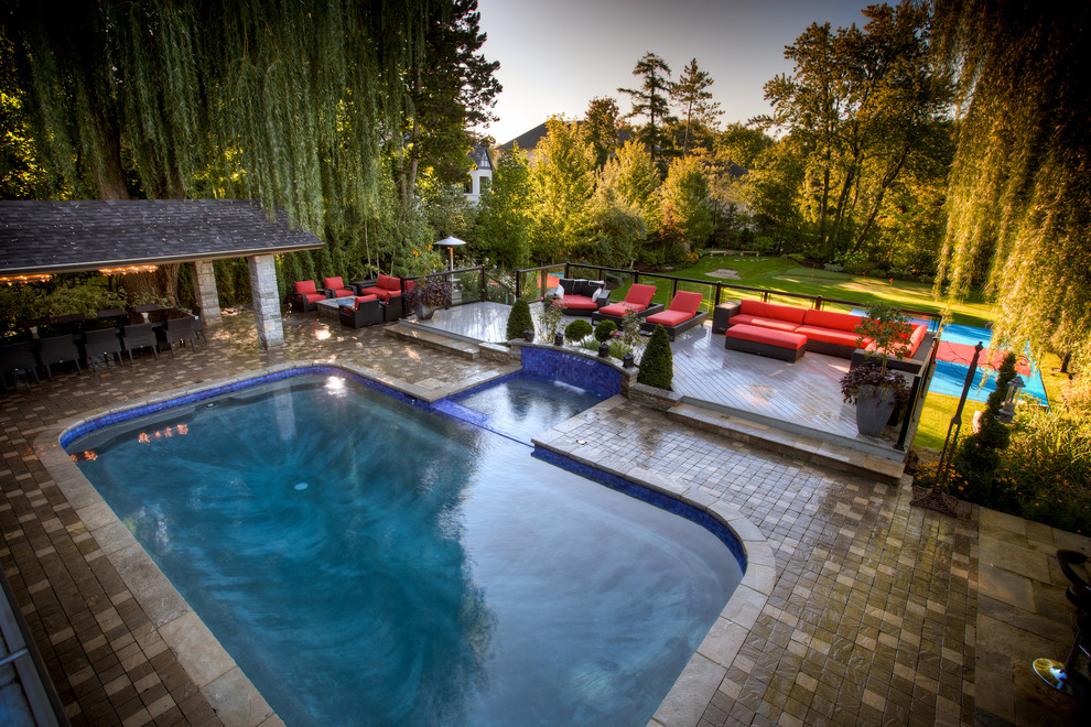 Diseño de piscina alargada clásica grande rectangular en patio trasero con adoquines de hormigón