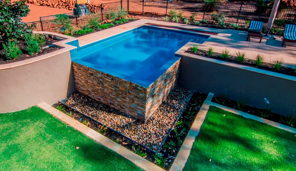 Diseño de piscina infinita de estilo de casa de campo de tamaño medio rectangular en patio trasero con adoquines de hormigón