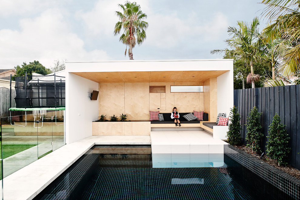 Modelo de casa de la piscina y piscina alargada actual rectangular en patio trasero con suelo de baldosas