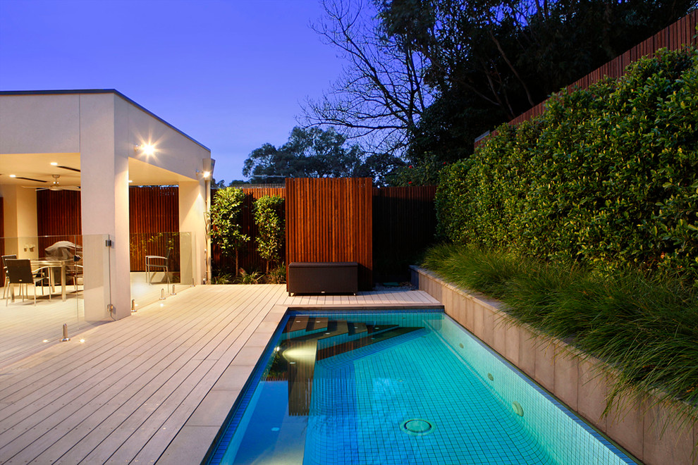 Diseño de piscina actual de tamaño medio rectangular en patio trasero con entablado