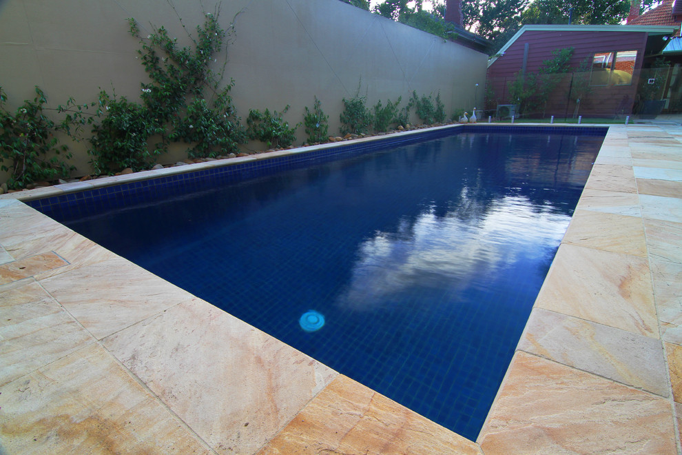 Ejemplo de piscina tradicional de tamaño medio rectangular en patio trasero con adoquines de piedra natural