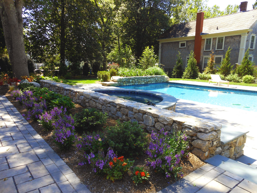 Aménagement d'une grande piscine latérale classique rectangle avec un bain bouillonnant et des pavés en béton.
