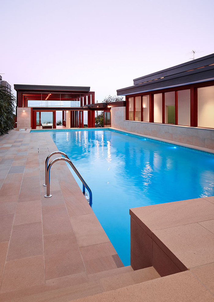 На фото: спортивный, угловой бассейн среднего размера на заднем дворе в стиле модернизм с домиком у бассейна и покрытием из каменной брусчатки