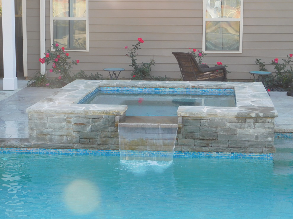 Exemple d'une grande piscine arrière tendance rectangle avec un bain bouillonnant et des pavés en pierre naturelle.