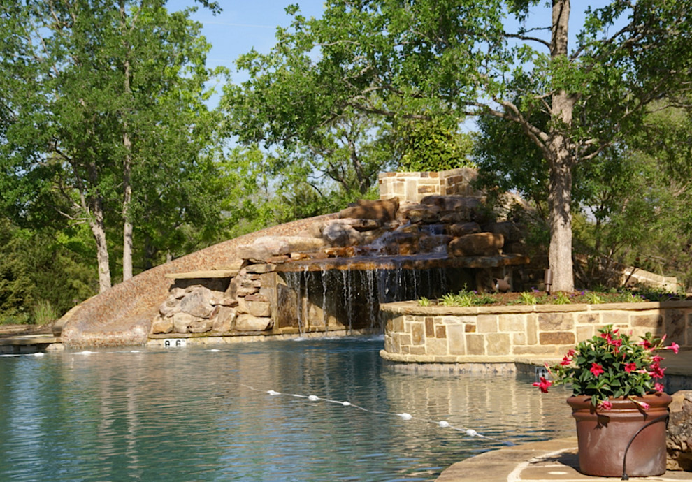 Large classic back custom shaped swimming pool in Houston with a water slide and concrete paving.