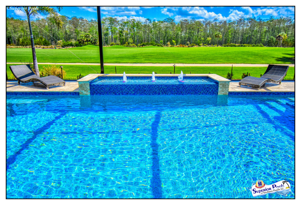 Foto de piscina con fuente alargada tropical grande a medida en patio trasero con adoquines de piedra natural