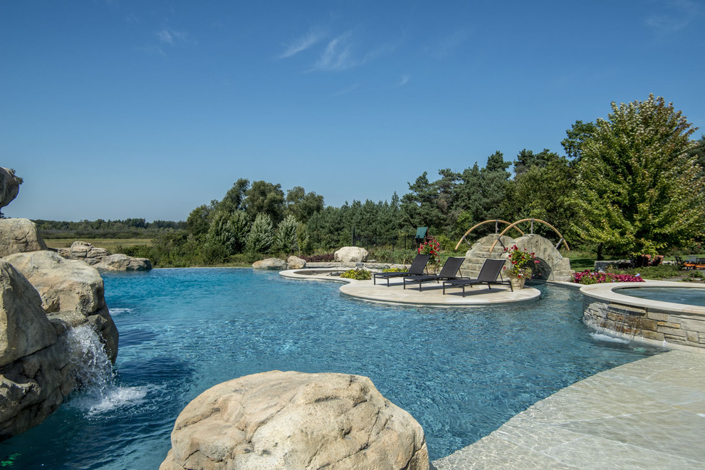 Ispirazione per un'ampia piscina a sfioro infinito personalizzata dietro casa con una vasca idromassaggio e pavimentazioni in pietra naturale