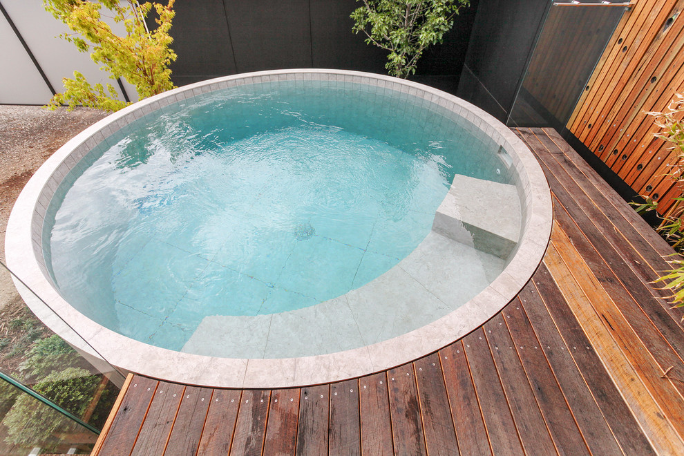 Diseño de piscina elevada actual de tamaño medio redondeada en patio trasero con entablado