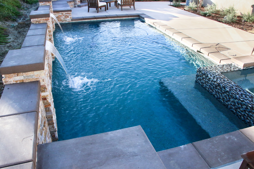 Ejemplo de piscina tradicional de tamaño medio rectangular en patio trasero con losas de hormigón