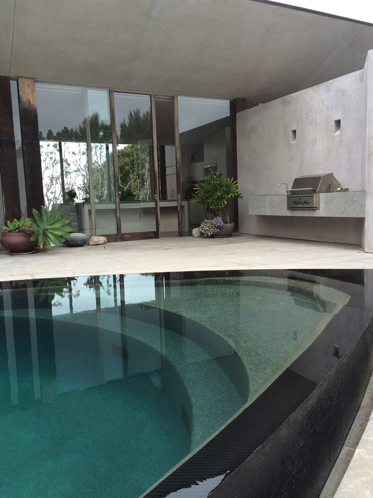Aménagement d'une grande piscine à débordement et arrière contemporaine sur mesure avec des pavés en pierre naturelle.