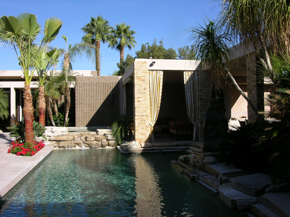 Ejemplo de piscina natural mediterránea grande en forma de L en patio con adoquines de piedra natural