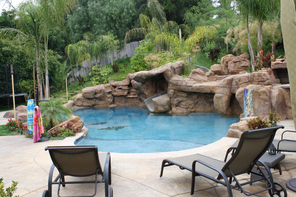 Diseño de piscina con tobogán natural exótica grande a medida en patio trasero con suelo de hormigón estampado