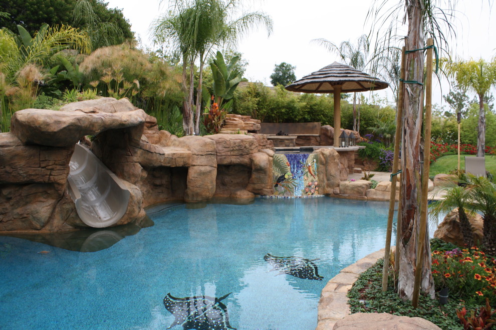 На фото: большой естественный бассейн произвольной формы на заднем дворе в морском стиле с водной горкой и покрытием из каменной брусчатки