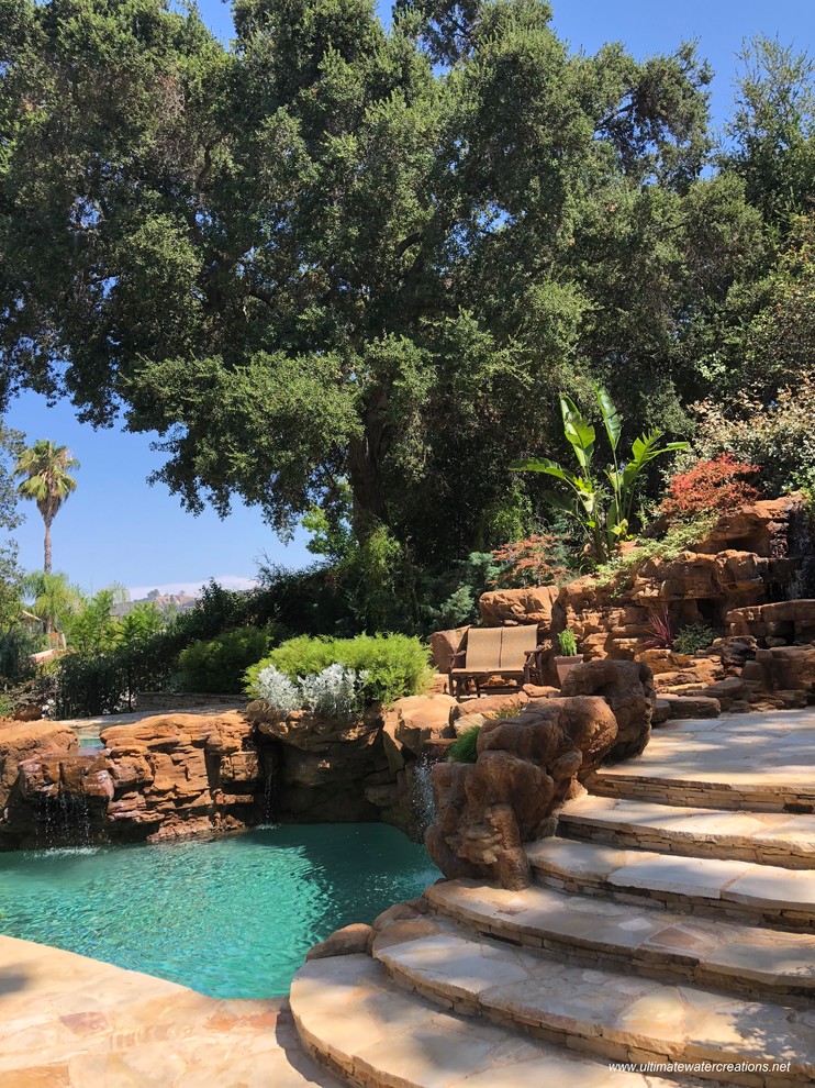 This is an example of a large world-inspired back kidney-shaped swimming pool in Los Angeles with natural stone paving.