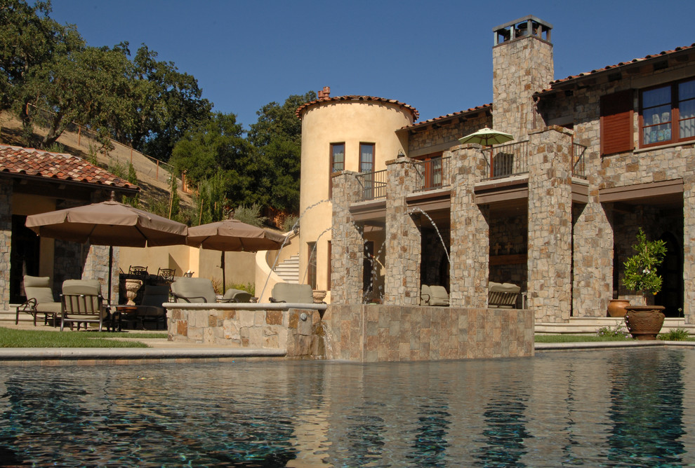 На фото: большой прямоугольный бассейн-инфинити на заднем дворе в стиле рустика с фонтаном и покрытием из каменной брусчатки