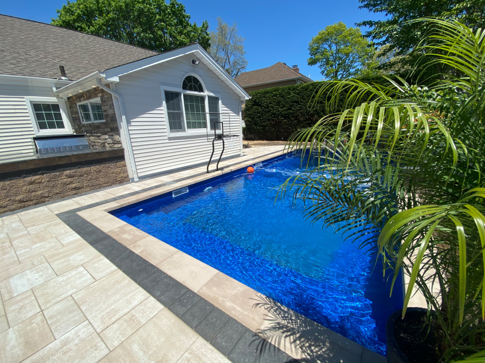 Modelo de piscina alargada contemporánea grande rectangular en patio trasero con paisajismo de piscina y adoquines de hormigón