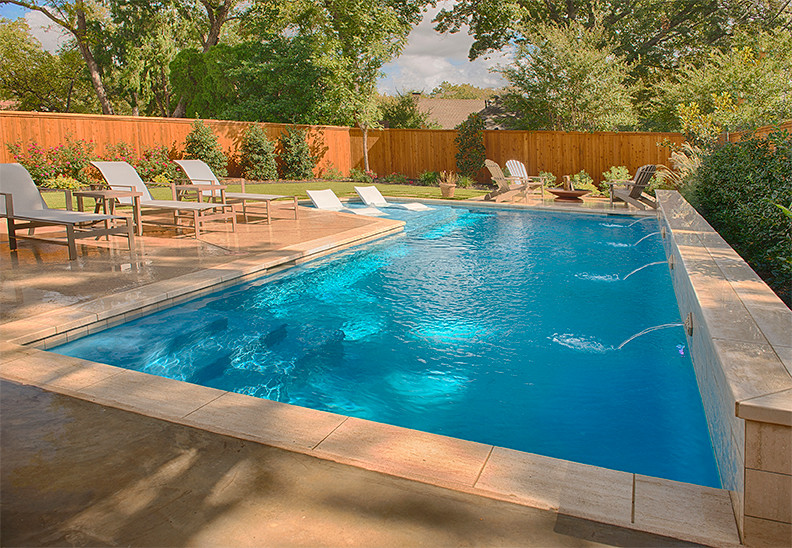 Modelo de piscina natural tradicional renovada de tamaño medio en forma de L en patio trasero con adoquines de hormigón