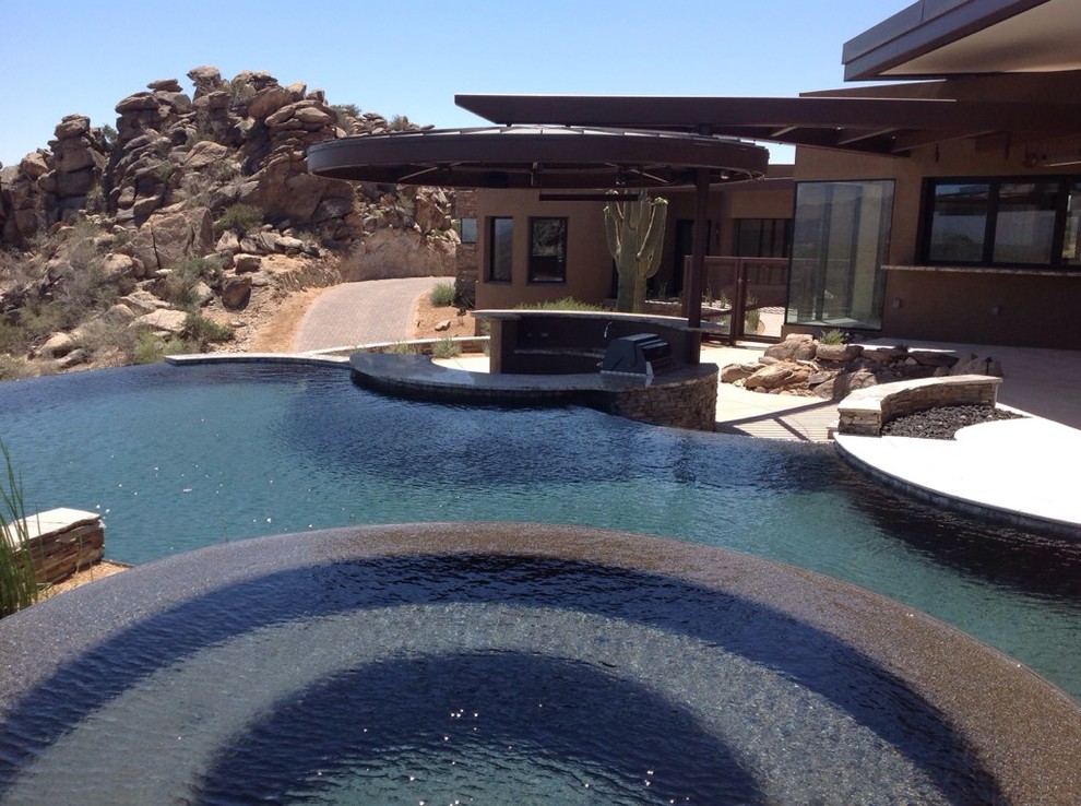 Imagen de piscina infinita actual grande a medida en patio trasero con adoquines de piedra natural