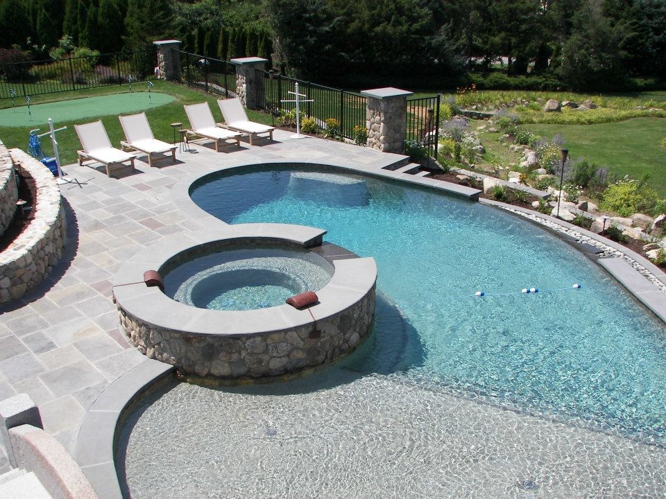 Cette image montre une grande piscine à débordement et arrière chalet sur mesure avec des pavés en pierre naturelle et un bain bouillonnant.