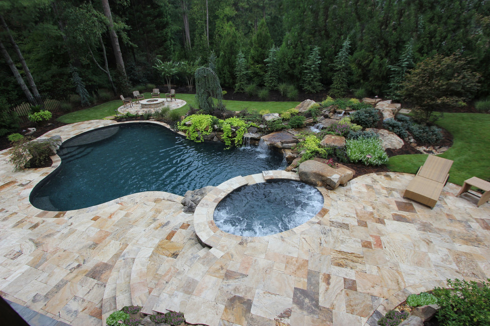 На фото: большой естественный бассейн в форме фасоли на заднем дворе в классическом стиле с джакузи и покрытием из каменной брусчатки
